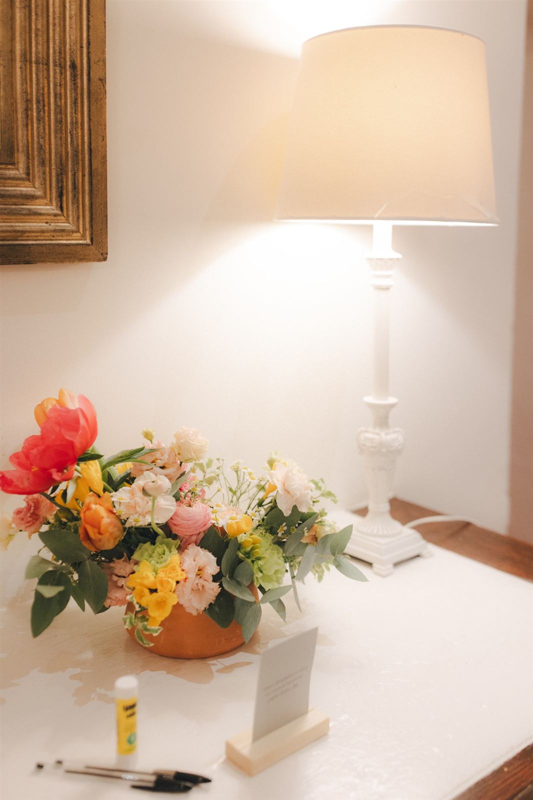Arranjo de peónias e flores amarelas junto a um candeeiro