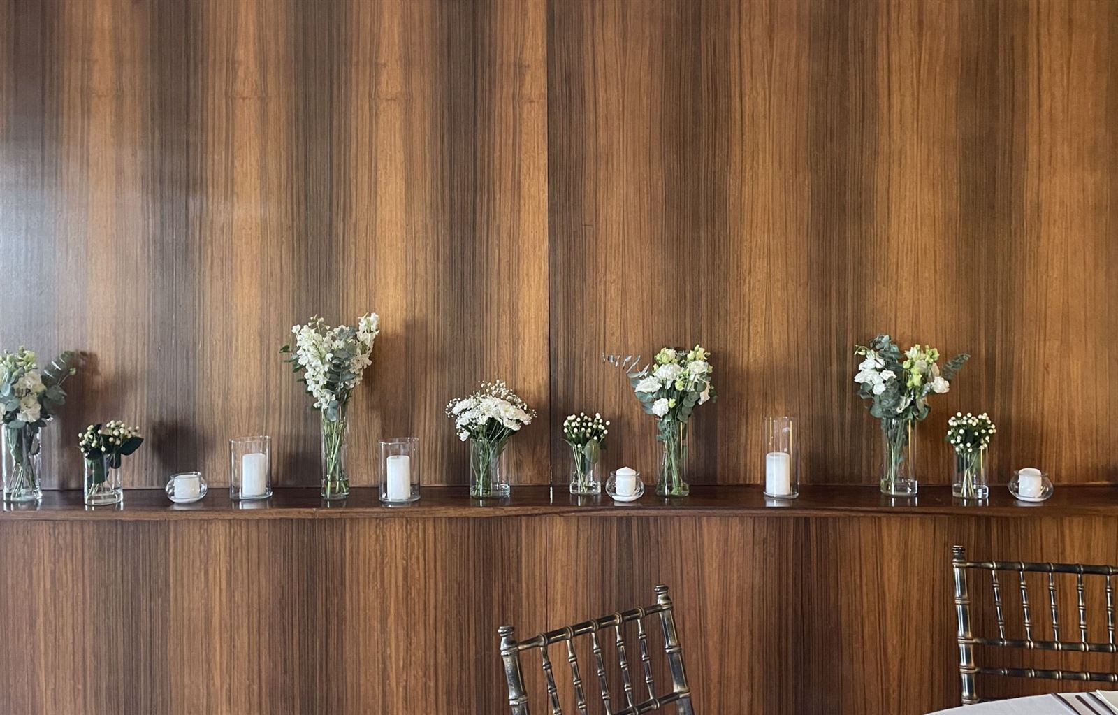 Jarras de flores brancas e velas ao longo de um painel de madeira